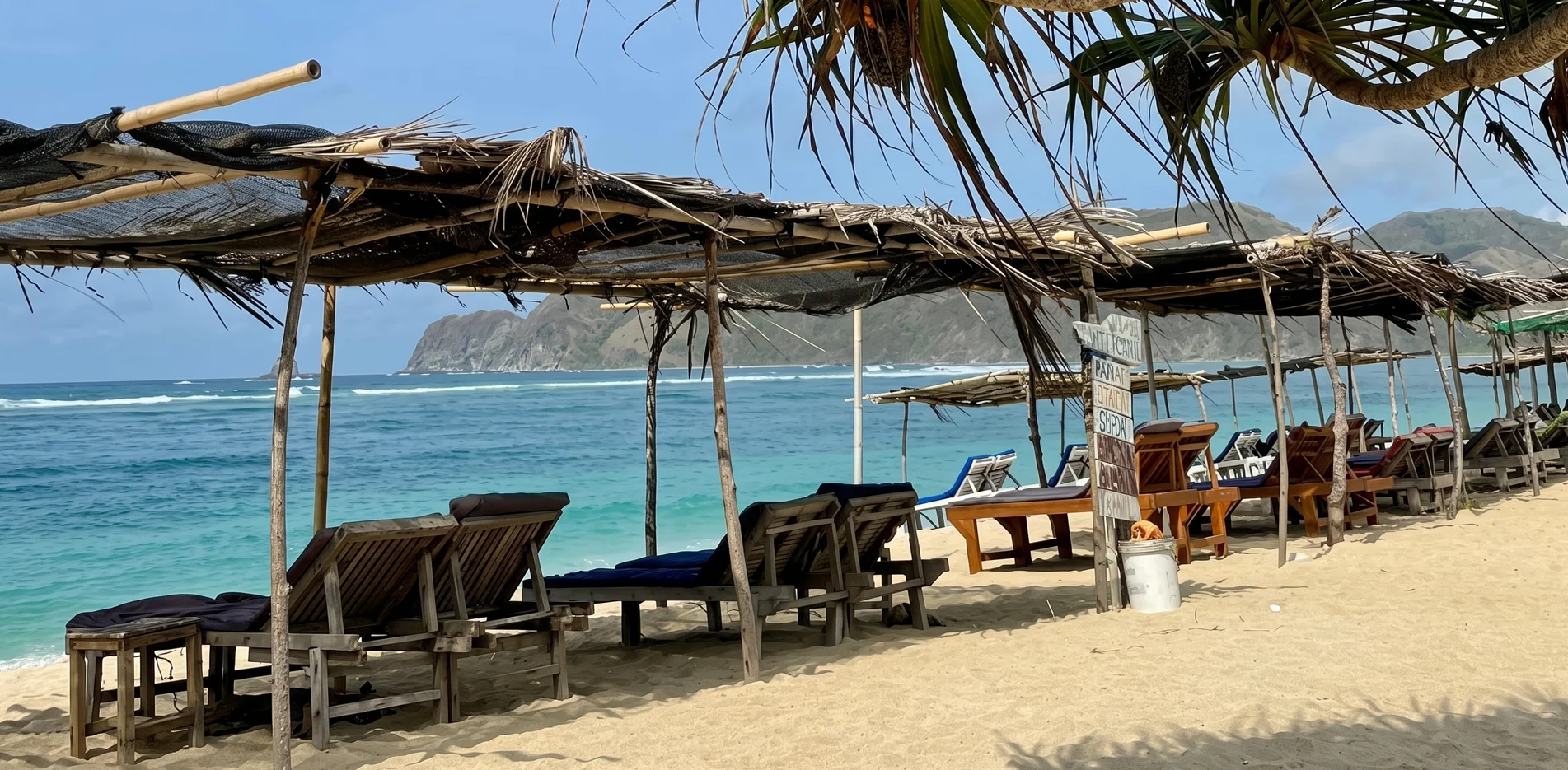 Sun loungers under a simple palm-leaf shelter facing the turquoise water at Tampah Beach