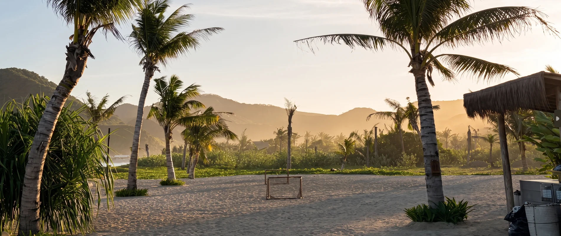 Beach football field framed by palm trees and hills in late-afternoon light near Tampah Beach